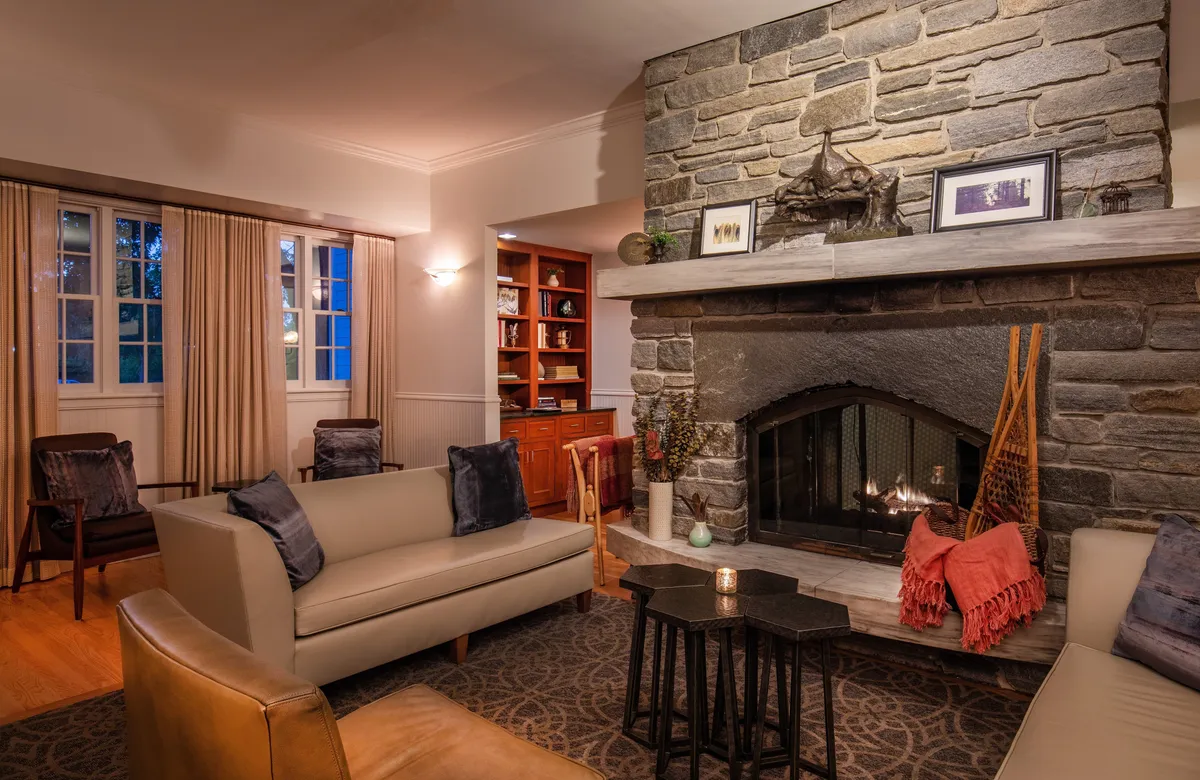 A cozy interior scene focused on a stone fireplace, with a comfortable sofa and coffee table nearby. The warm ambiance invites guests to unwind, socialize, or enjoy a quiet moment by the fire, evoking relaxation and comfort, especially after outdoor adventures or while enjoying seasonal amenities like s’mores.