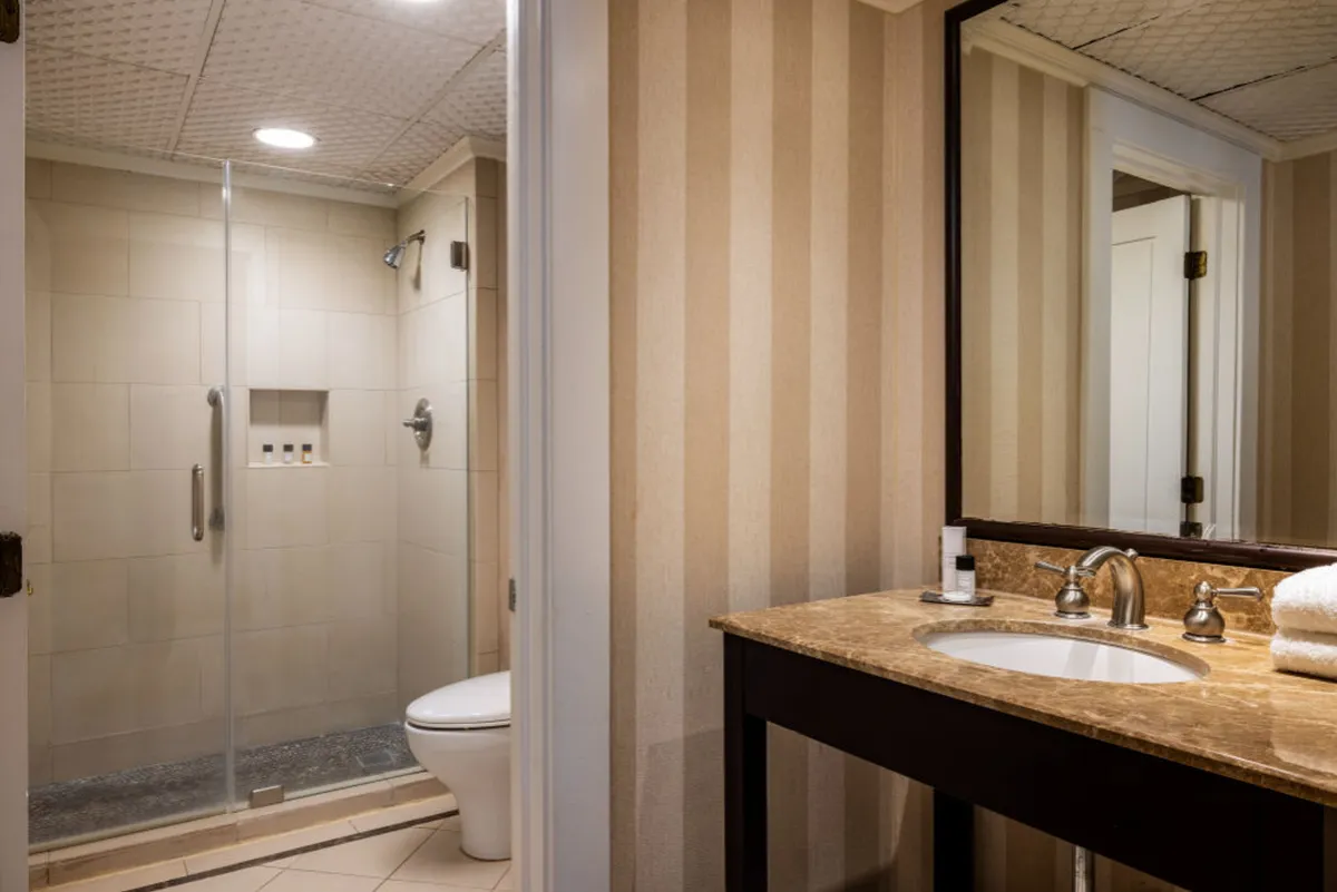 A serene bathroom interior featuring a glass shower enclosure, marble countertop, and striped wallpaper. The space exudes tranquility and modern comfort, designed for personal grooming and relaxation.