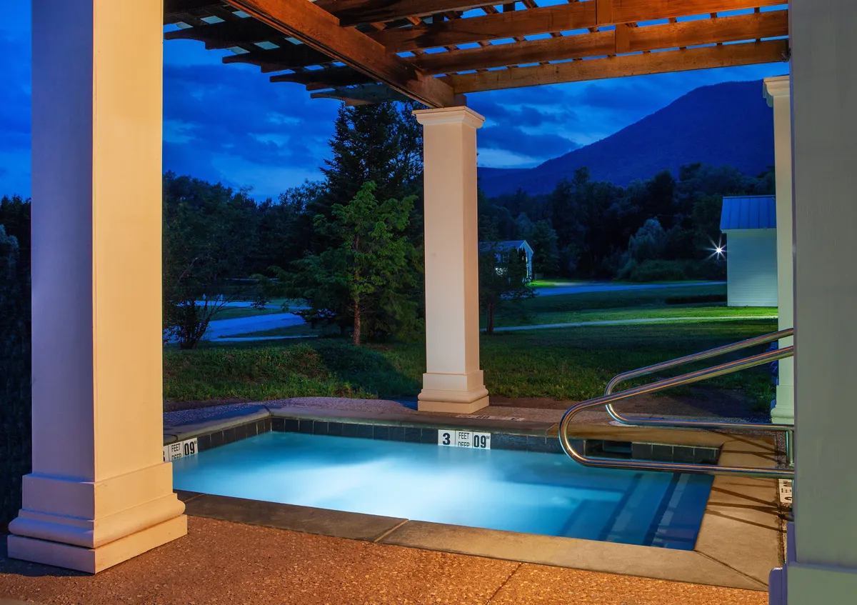 A serene heated swimming pool sits at the forefront, framed by an elegant pergola. Beyond the pool, panoramic views of the Green Mountains stretch into the distance, creating a tranquil setting ideal for both relaxation and social gatherings. The scene suggests a perfect place for couples or luxury travelers to unwind and take in the natural beauty.